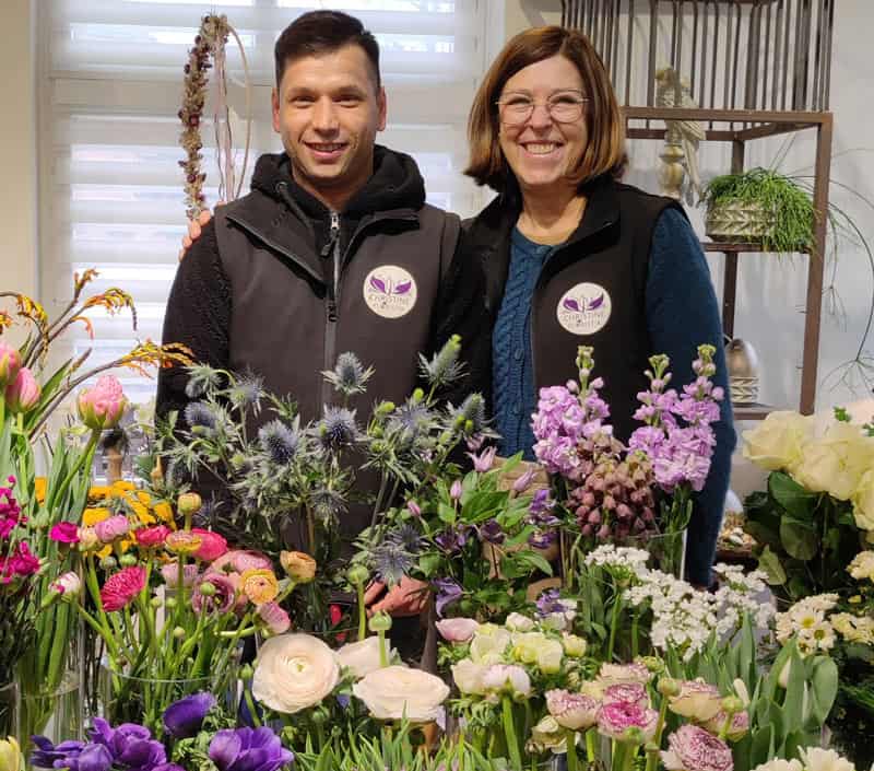 Geschäftsführerin Christine Heuer mit ihrem Angestellten Jungflorist Said Farid. dem 2. platzierten des MDR Garten-Florist 2023 Wettbewerbs. Davor viele verschiedene Blumen.